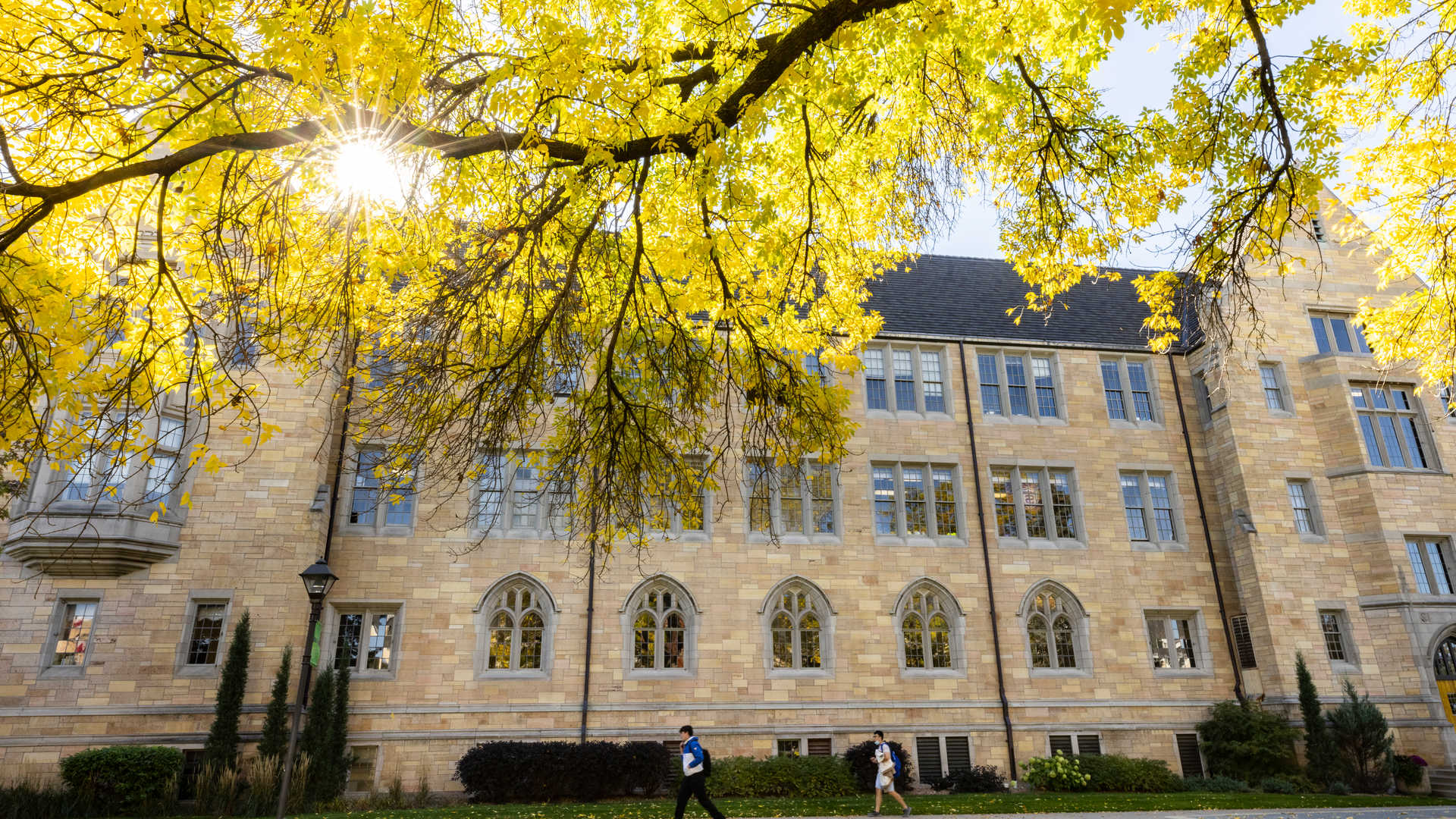 a student walks past Aquinas Hall with fall leaves overhead