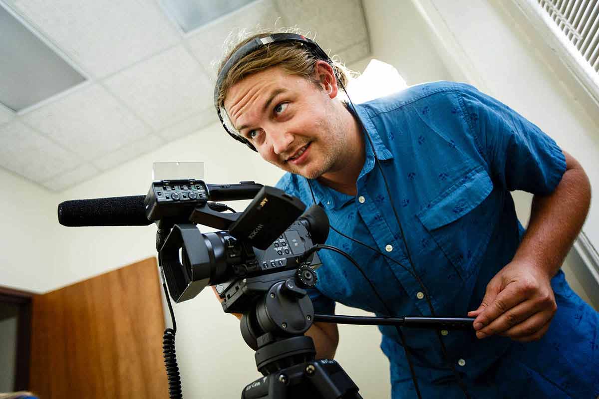 Zachary Neubauer operates a video camera during a staged film production.