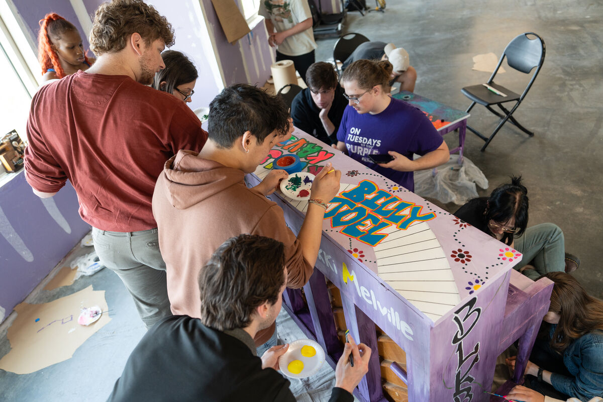 Students painting a wooden upright piano.