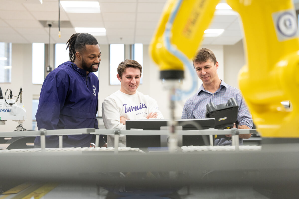 Professor giving a demonstration to two students in a robotics automation lab.