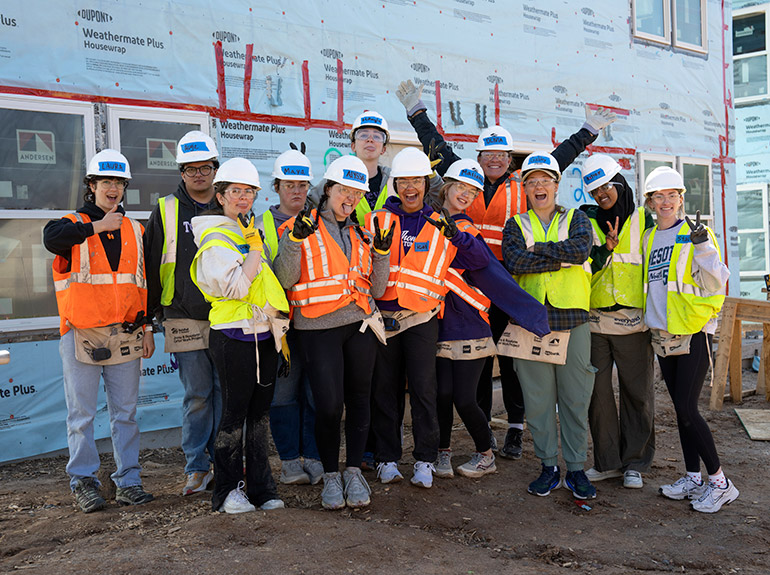 A group of students in hard hats and safety vests volunteer at Habitat for Humanity