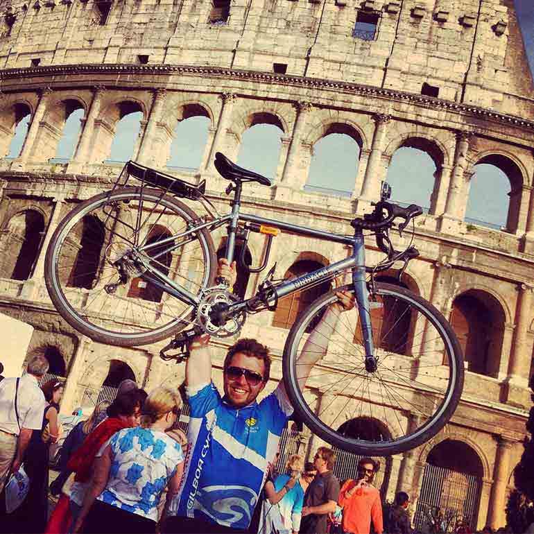 Student hoists bicycle in air in front of the colosseum in rome, italy