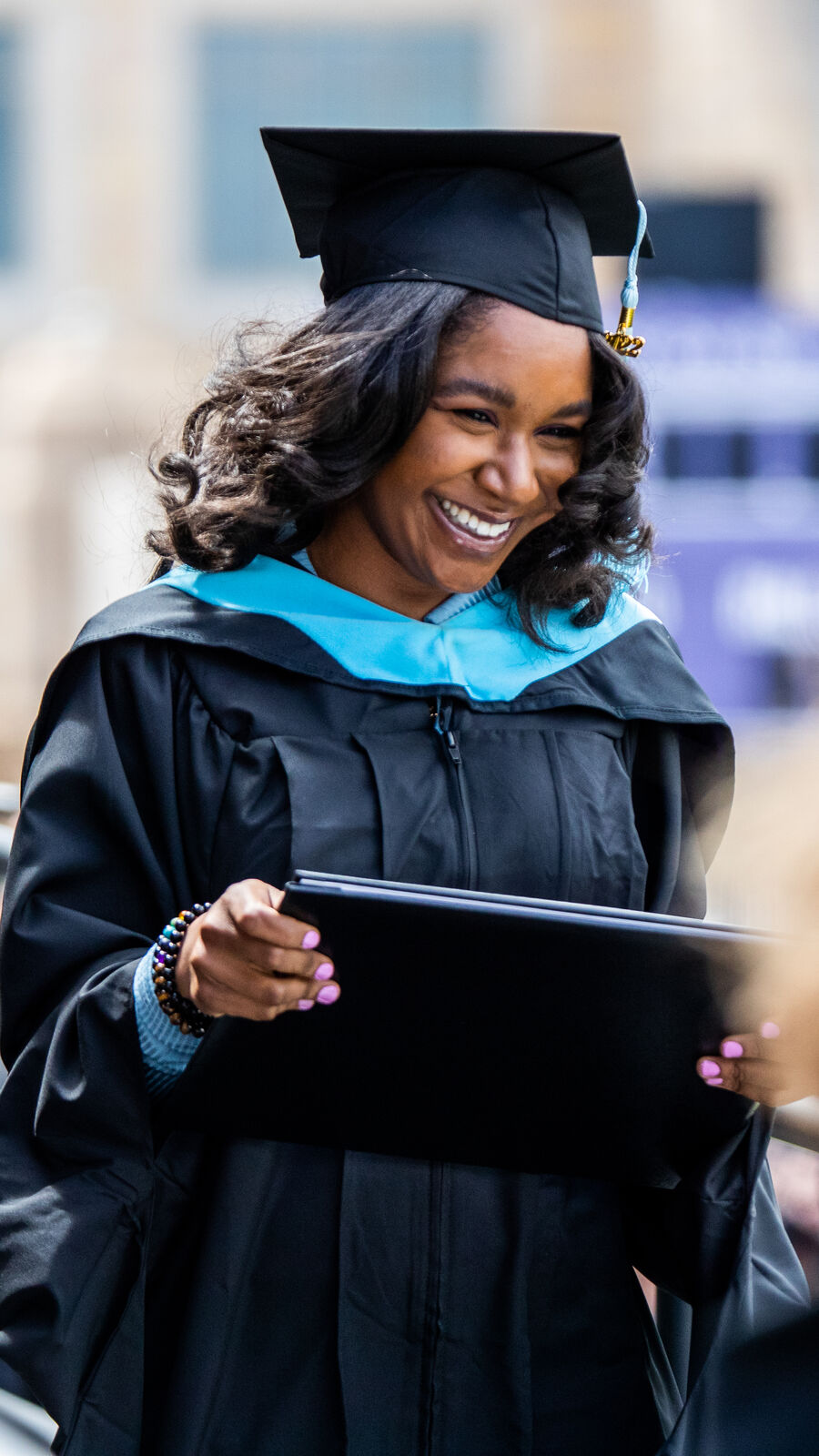 Student smiling in cap and gown, walking across a stage during graduation ceremony.