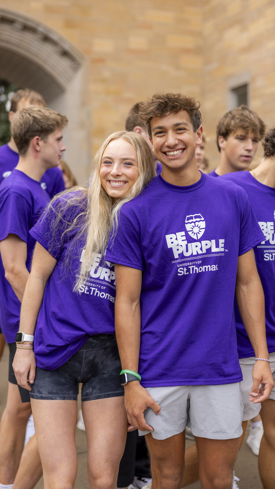 Two students standing together and smiling outside in a crowd.