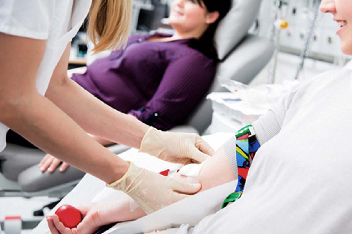Woman with gloved hands takes blood during blood drive.