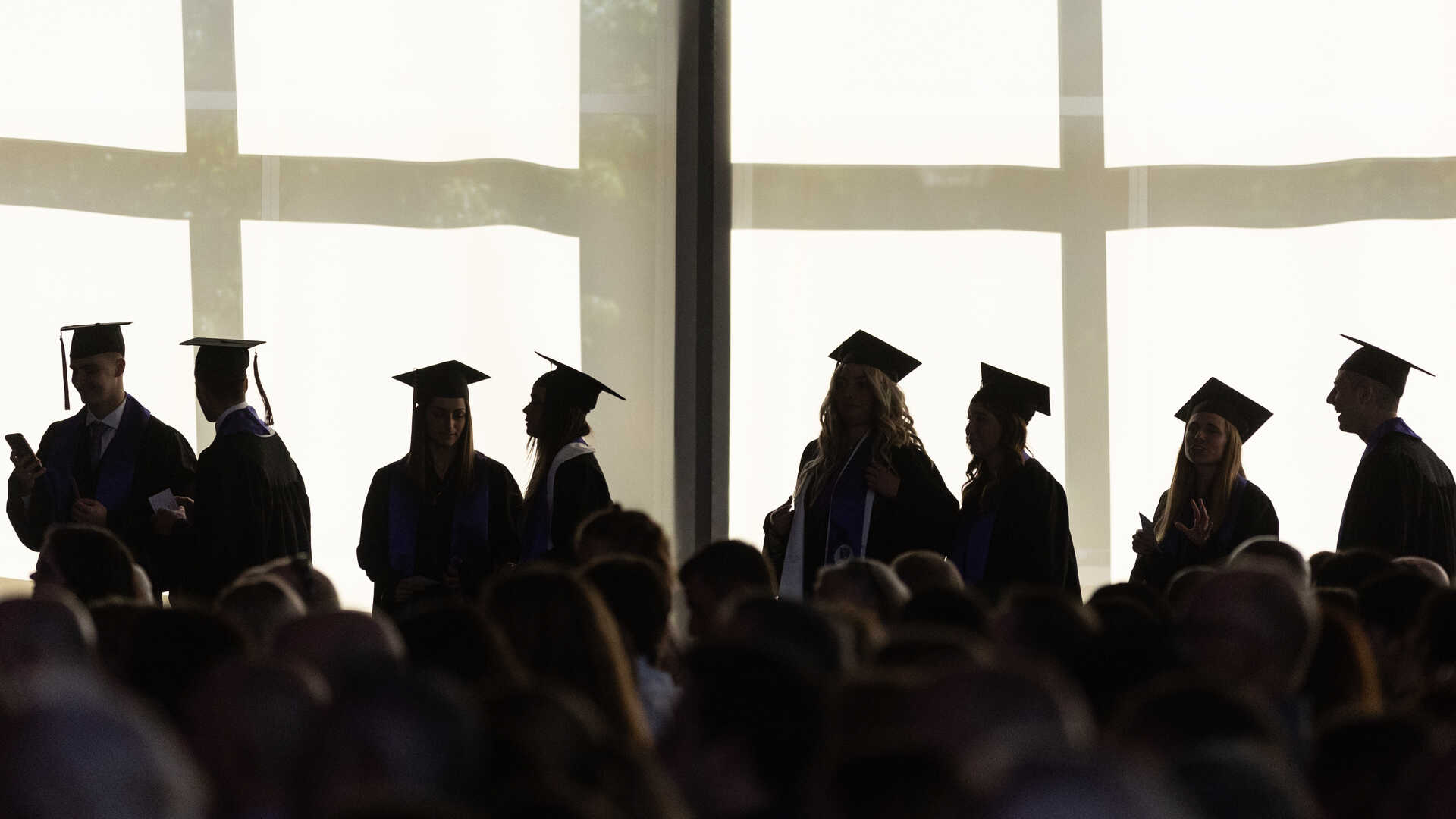 a group of graduates silhouetted in front of windows