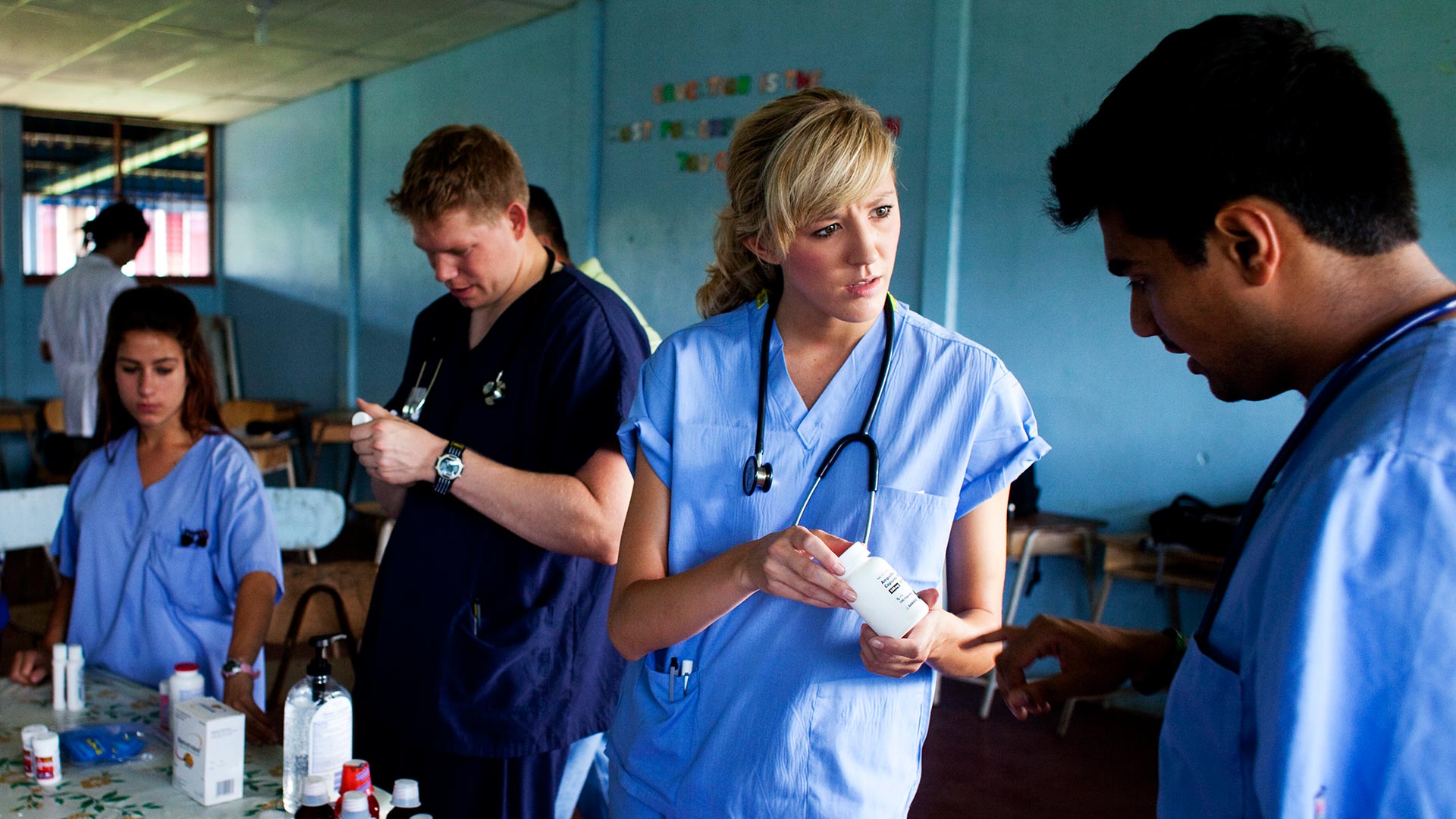 Students with stethoscopes discuss and examine bottles of medication