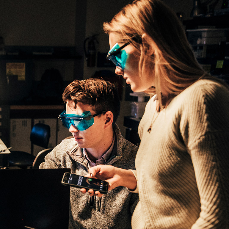 Students work in a lab while wearing safety glasses.