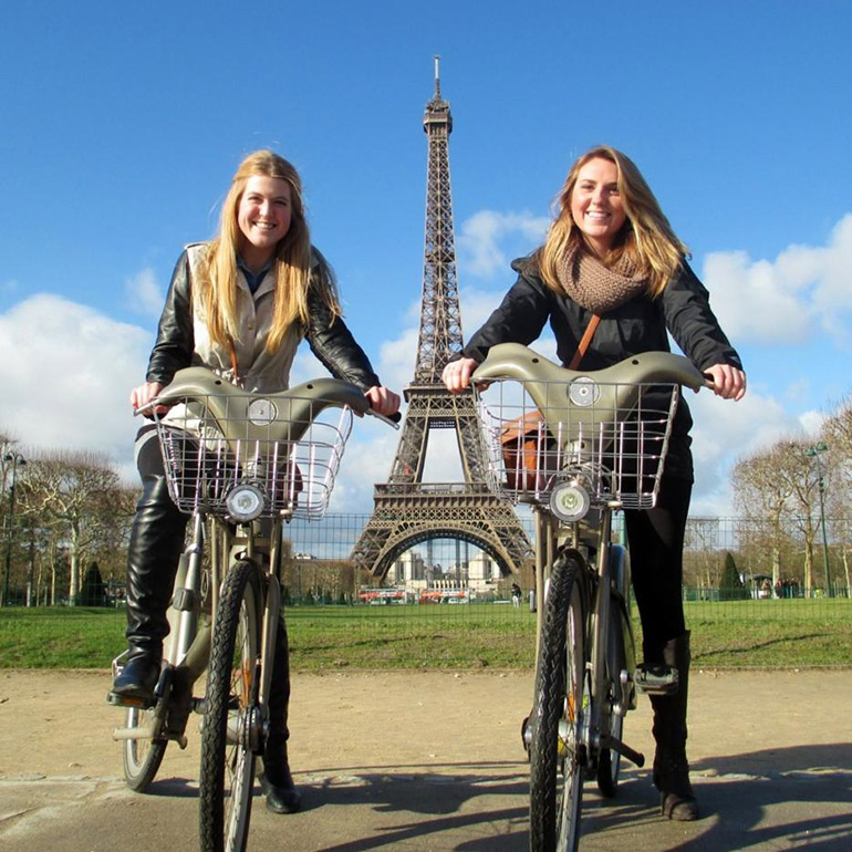 Two students on bicycles in Paris, France near the Eiffel Tower.