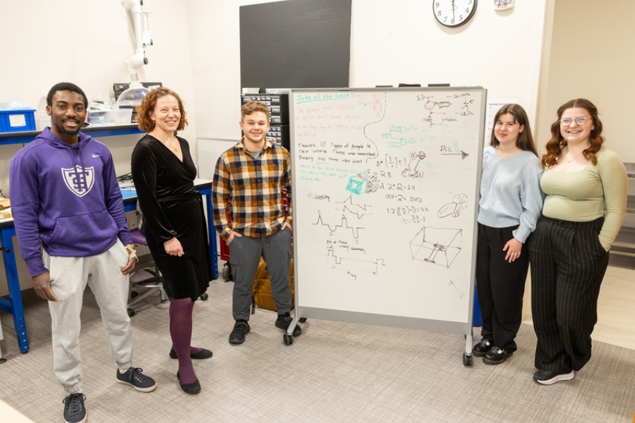 students and their professor pose next to a whiteboard of their math in an engineering lab