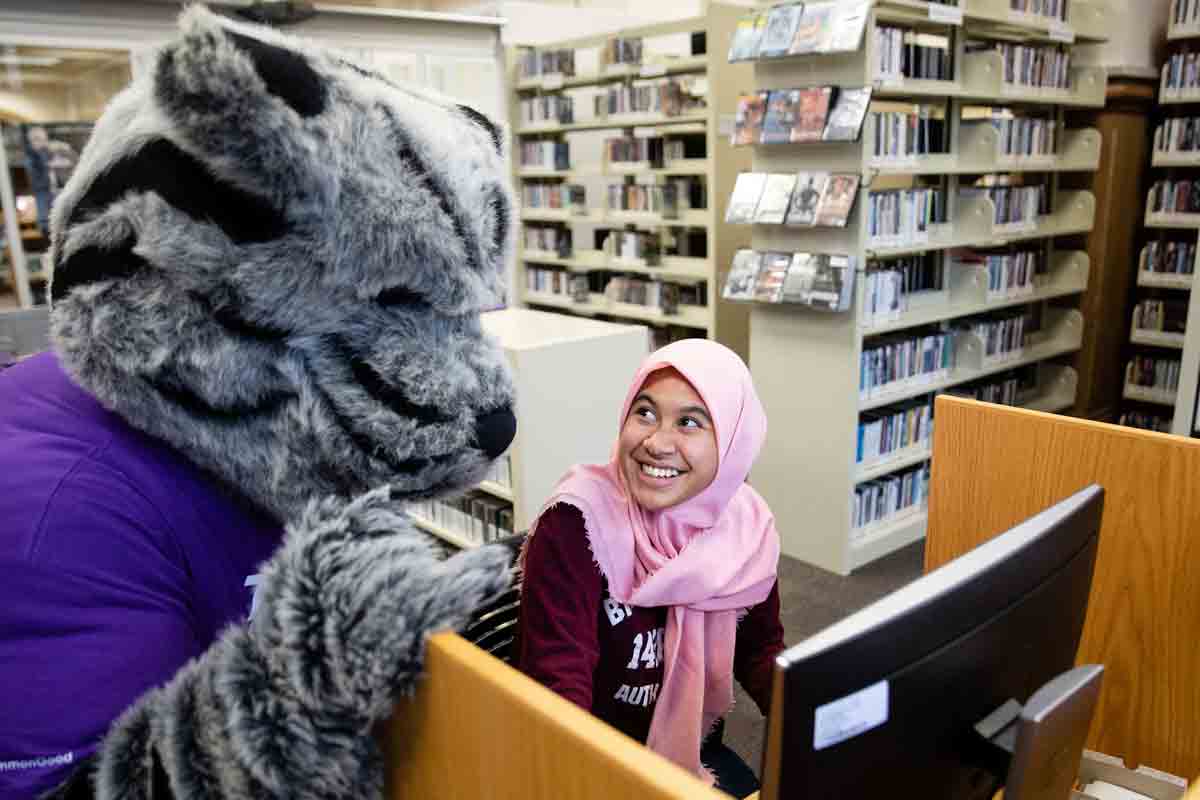 A female student works with mascot, Tommie on a computer.