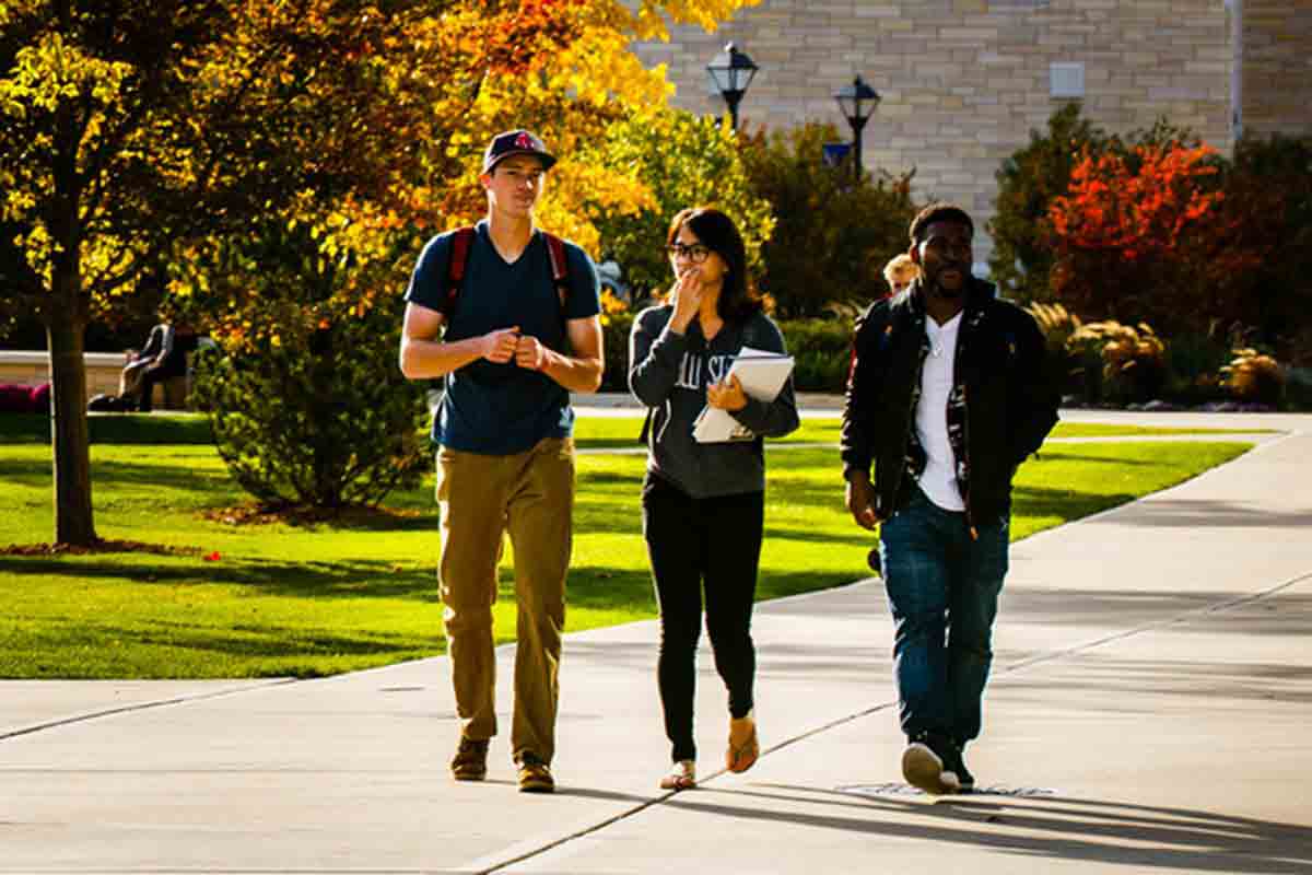 Students walk on campus with autumn foliage in the background.