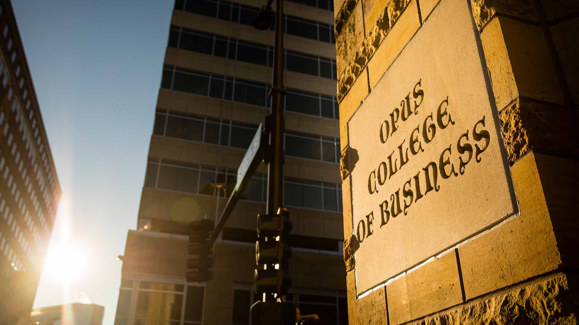 The sun sets beside the Opus College of Business sign.
