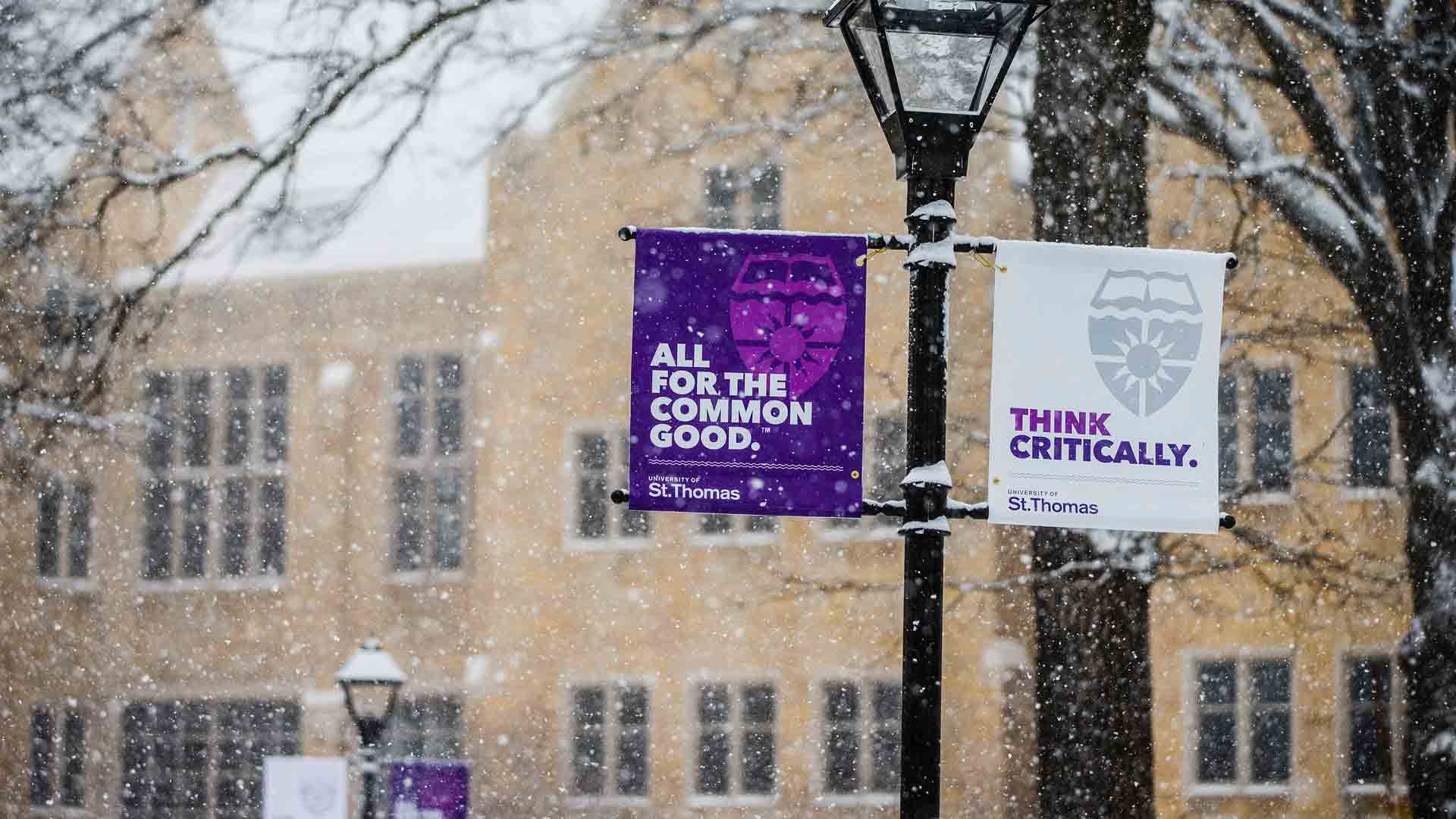 Two University of St. Thomas branded banners, the one on the left reads "All for the common good." The other banner has writing on it that says, "Think Critically."