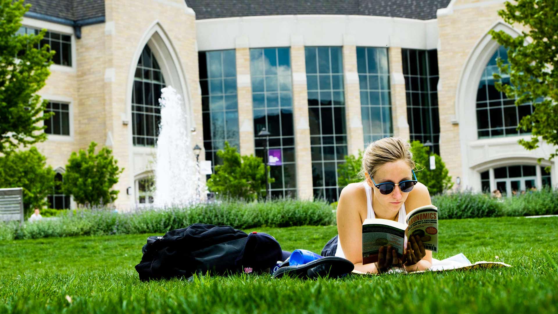 Female student reads book on grass of lower quad.
