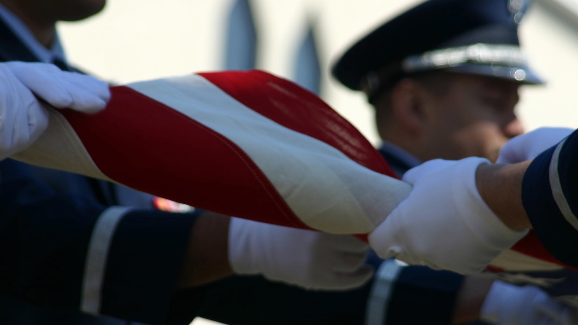 White gloved hands of military members folding U.S. flag.