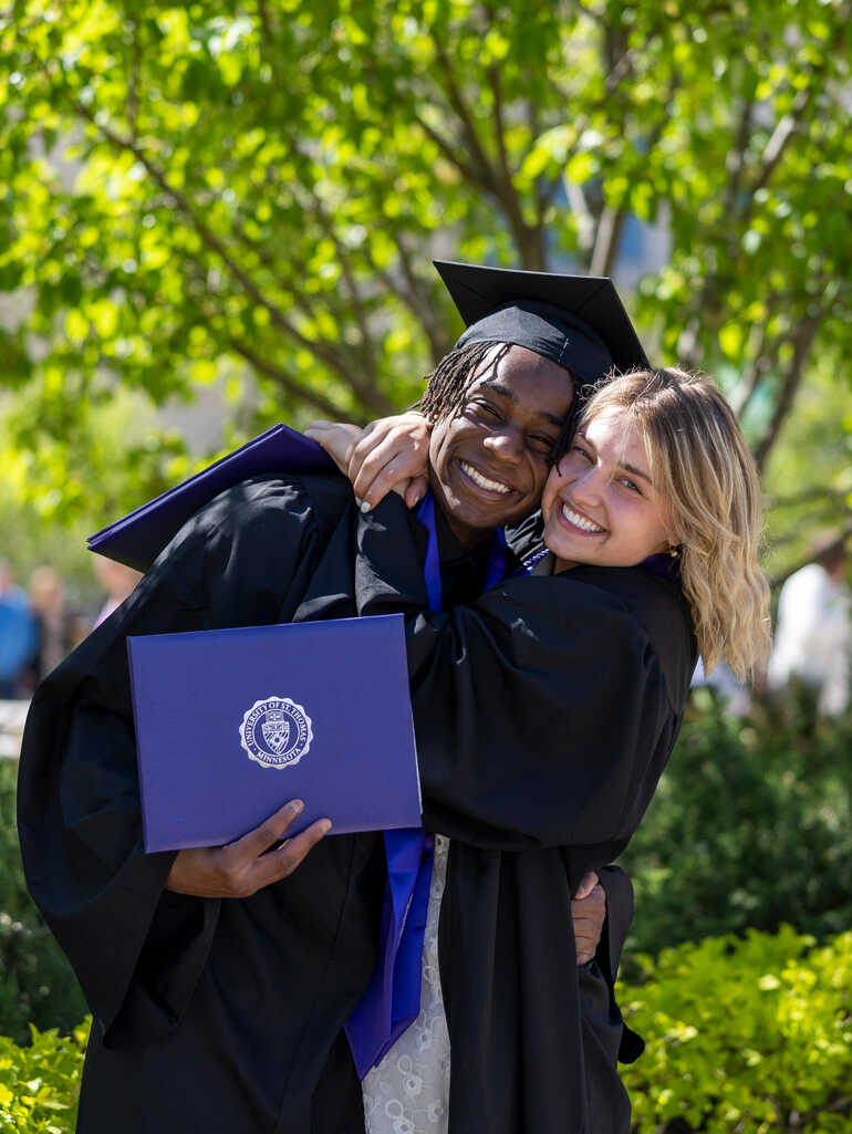 two students hugging and wearing graduation caps and gowns