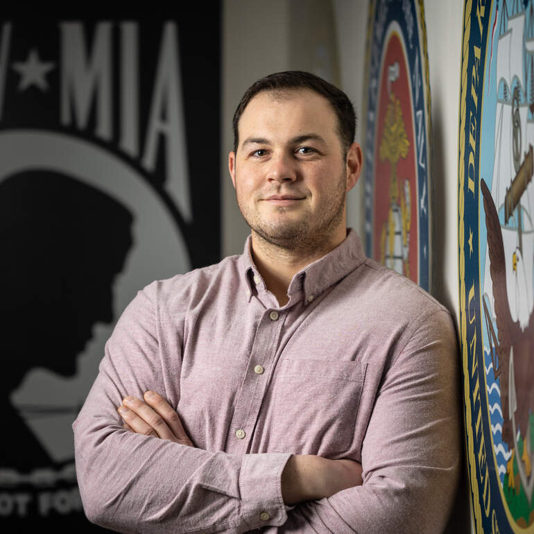 Eric Olson is standing in front of military logos in the veterans resource center