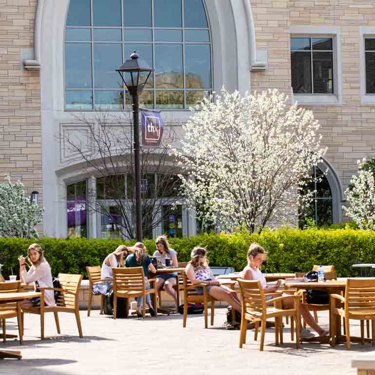 Students study outside in the spring at tables on Monahan Plaza.