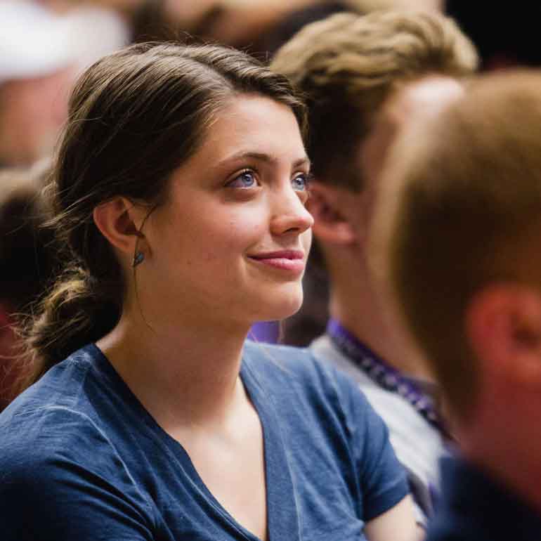Female student sits in audience and listens.