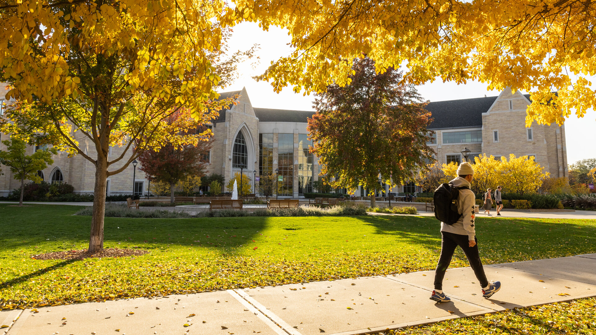 A student walking on campus surrounded by colorful autumn leaves