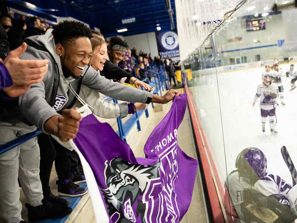 Students at a hockey game lean forward with a purple St Thomas flag