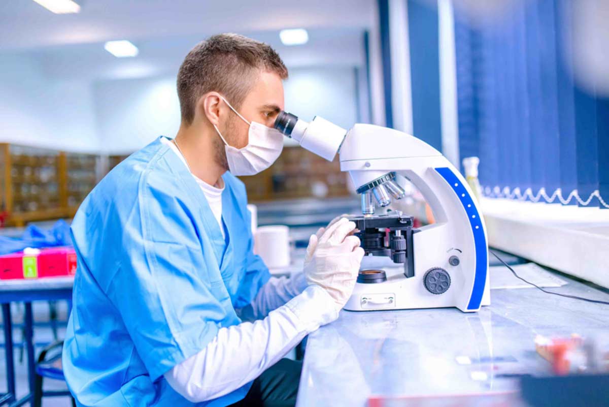 Person in scrubs and a mask looking into a microscope.