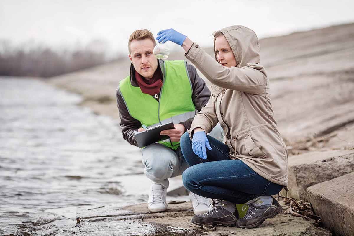 Two researchers analyze a water sample near a dam.
