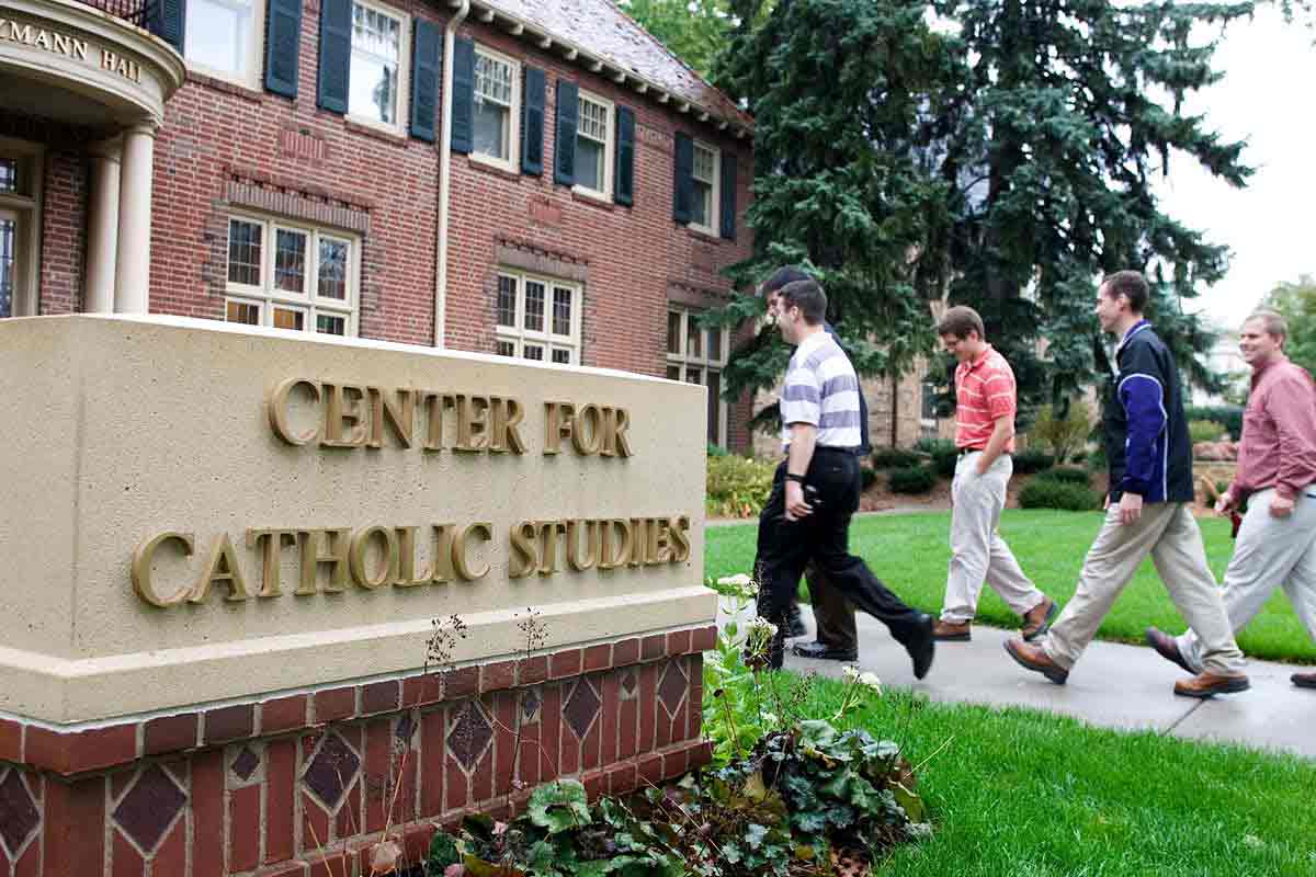 Students walk into Sitzmann Hall past a sign that reads "Center for Catholic Studies."