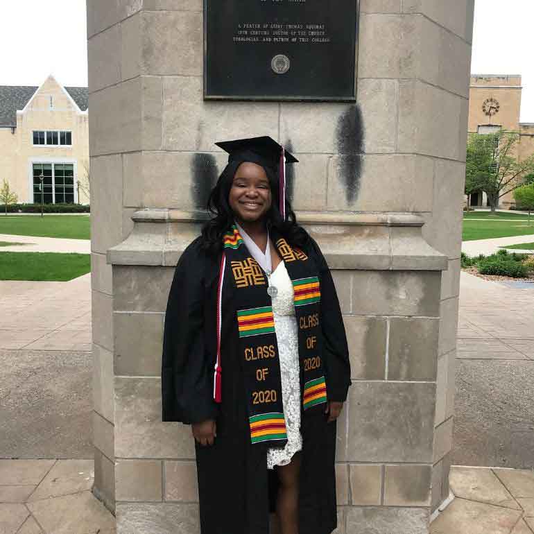 Chioma Uwagwu poses for a photo in front of the St. Thomas Arches in a cap and gown.