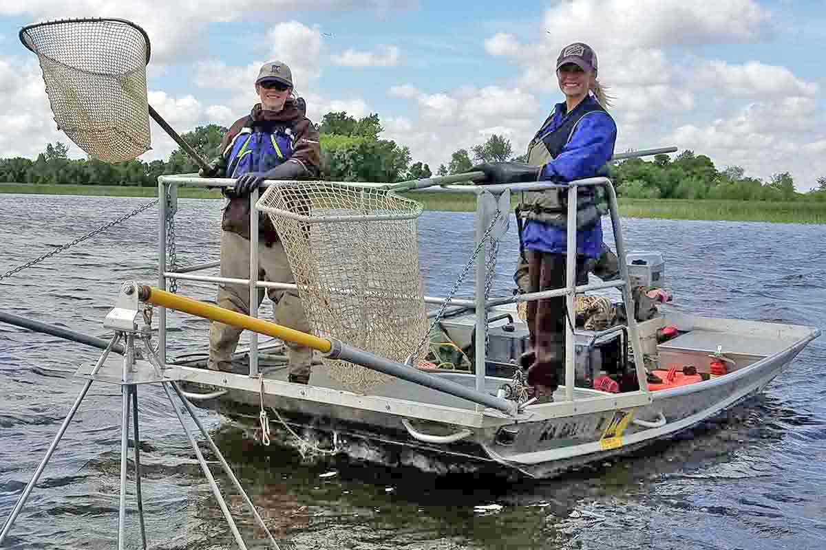 Environmental Science students on a  boat holding nets as they clean a river.