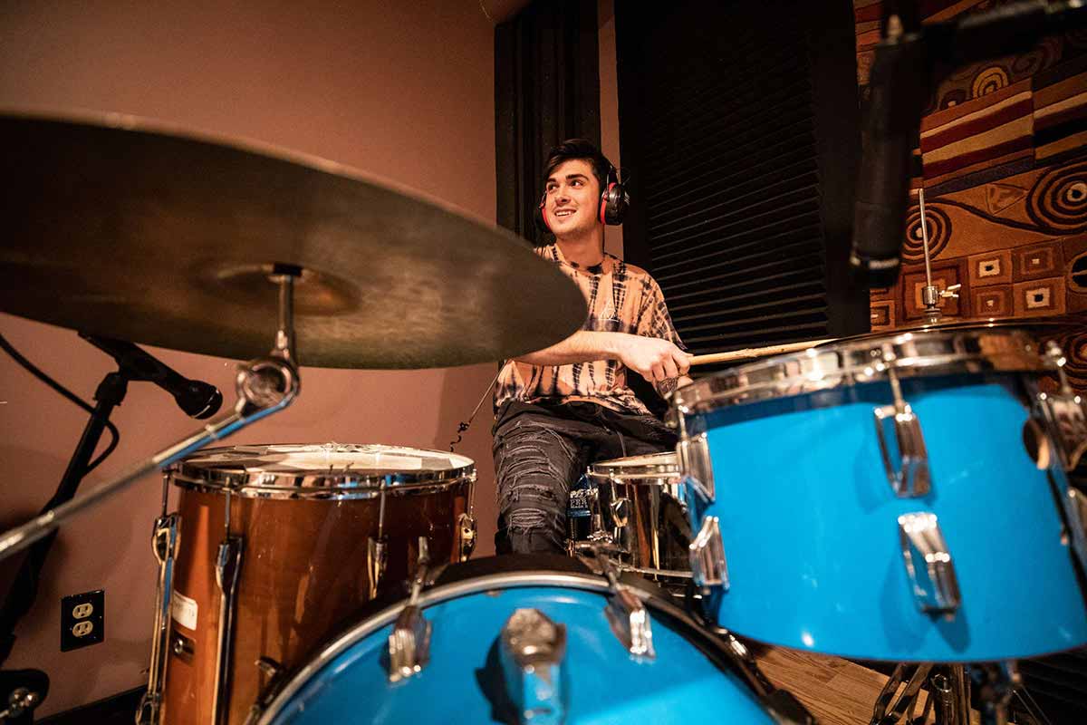 A student plays the drums in a recording studio.