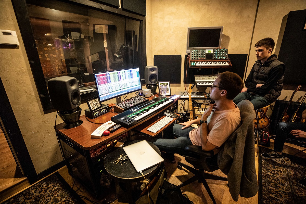 Two individuals produce music in a recording studio.