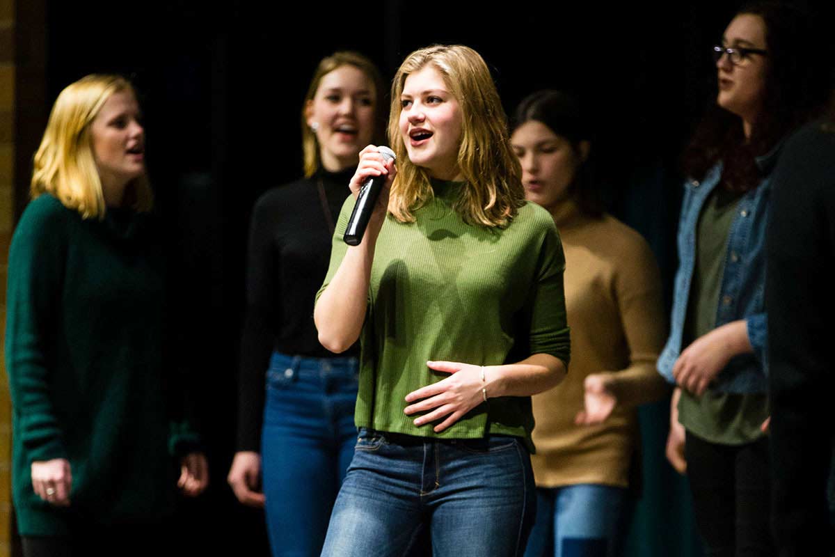 The women's a capella group Cadenza performs in an auditorium.