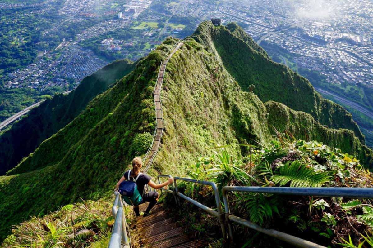 An individual on a green mountain looking down on the city below in Hawaii. 