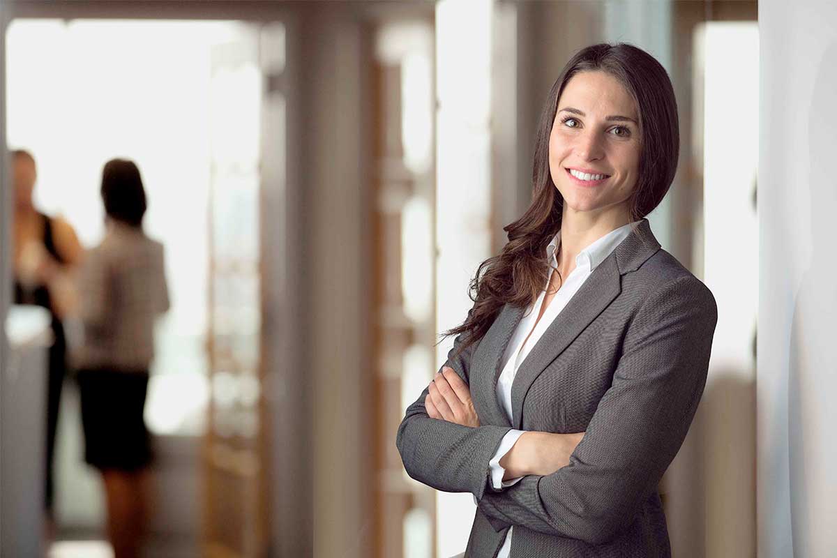 Business professional smiling with crossed arms in an office.
