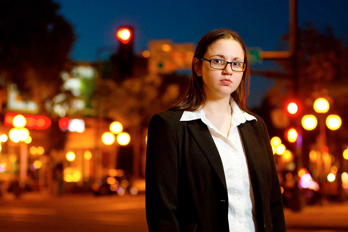 Sociology alumni poses for a portrait on dimly lit street corner.