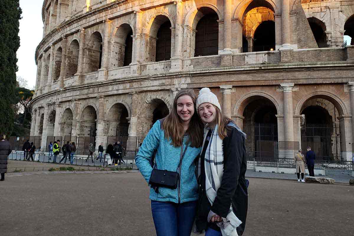 Two female students pose in front of the Rome Colosseum.