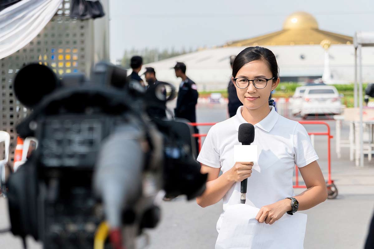 A woman news reporter speaking in front of a camera.
