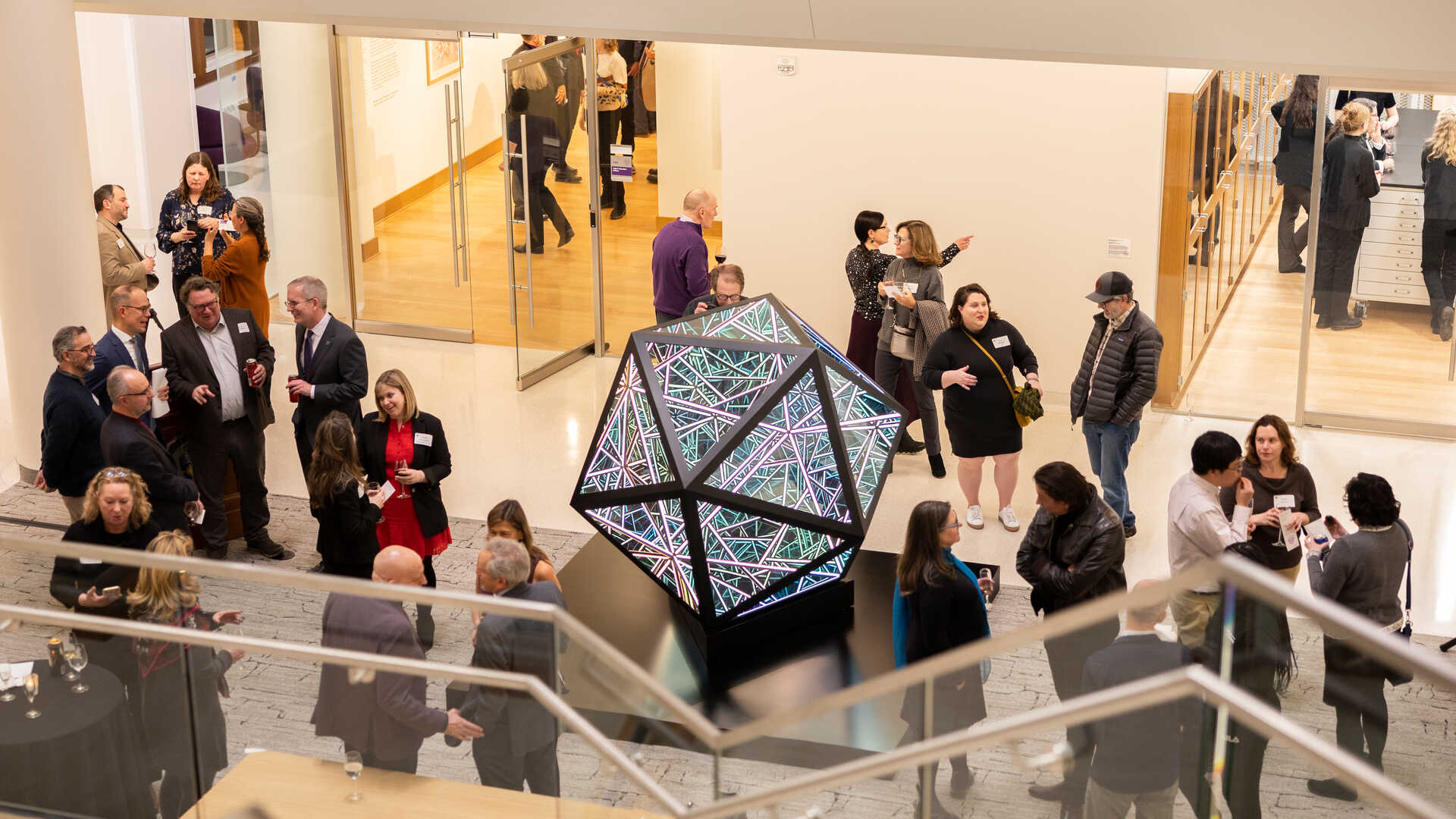 A crowd socializes next to the Anthony James Icosahedron sculpture