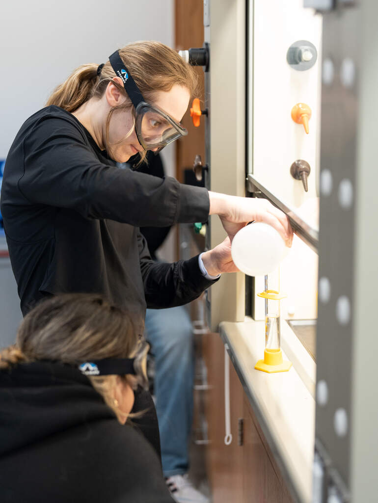 A student works with peers in a chemistry lab.