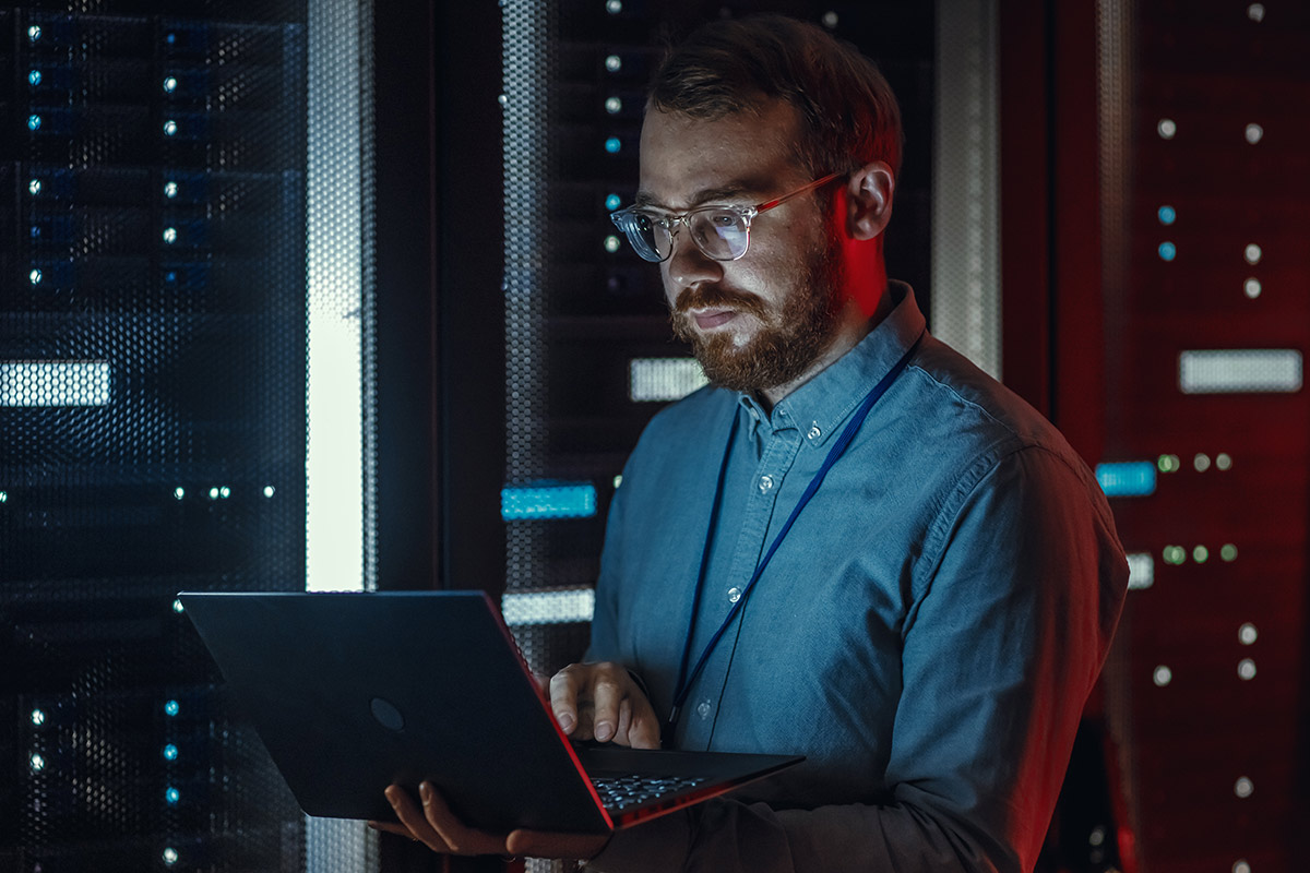 Person working on a laptop in a computer server room.