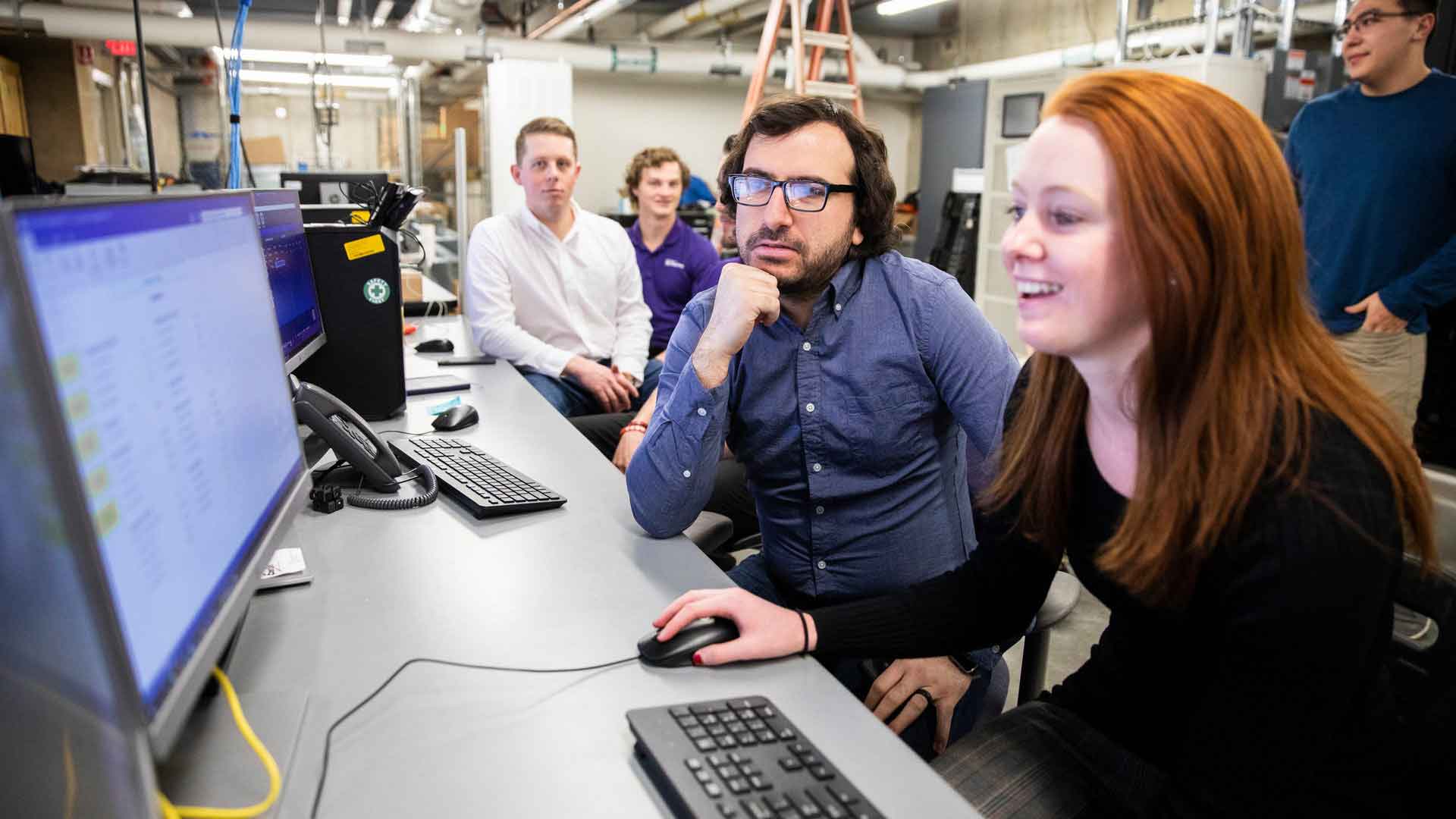 A group of electrical engineering student researchers and Dr. Mahmoud Kabalan work at a console in the Center for Microgrid Research.