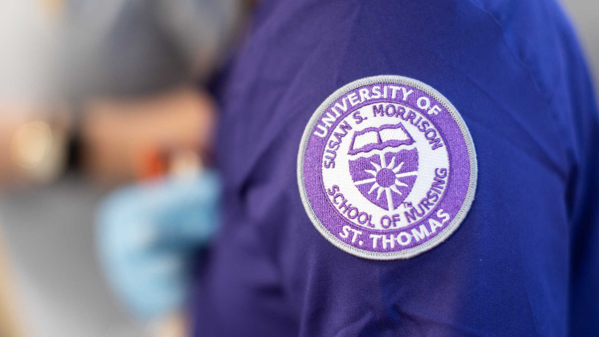 A person wearing scrubs with the School of Nursing badge
