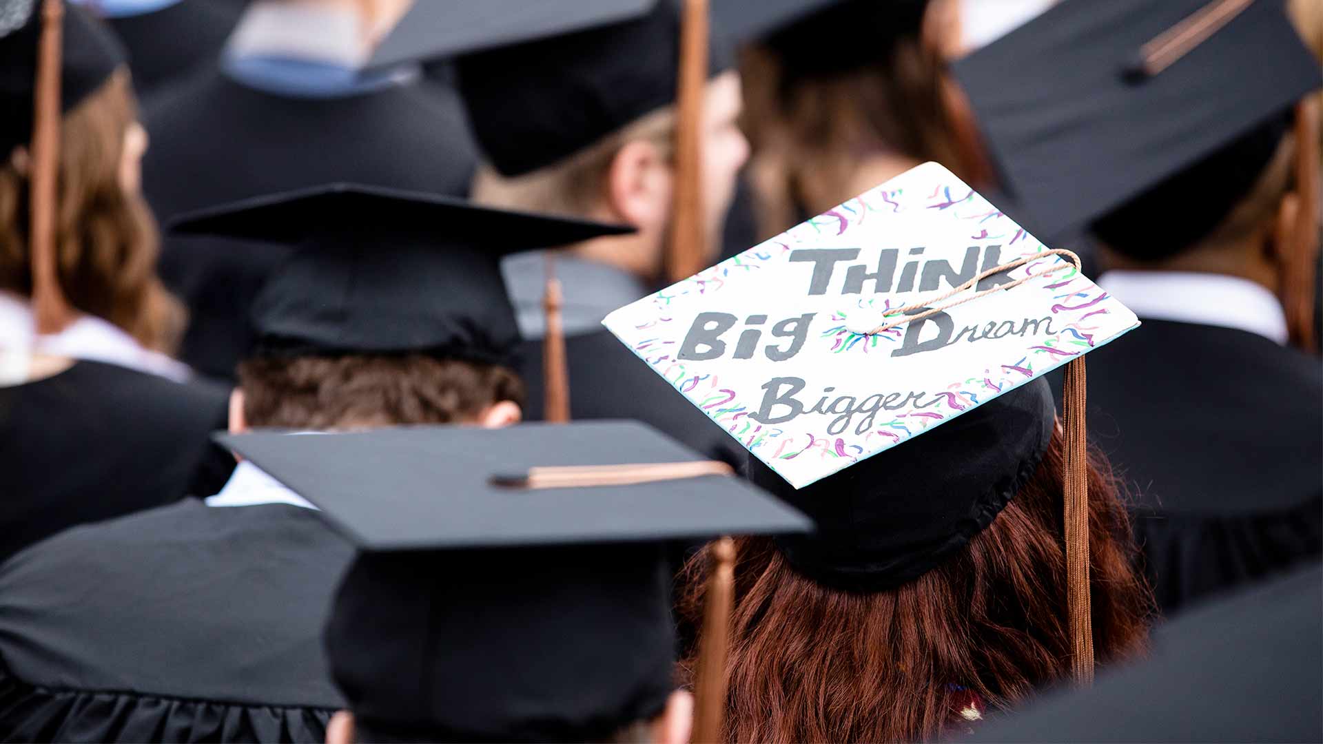 A student wears a graduation cap that has the words, "Think Big, Dream Bigger," written on it.