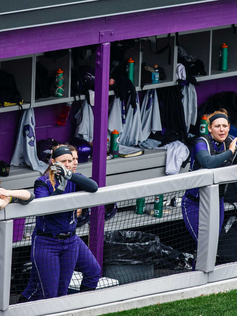 Tommies stand in the dugout during a softball game