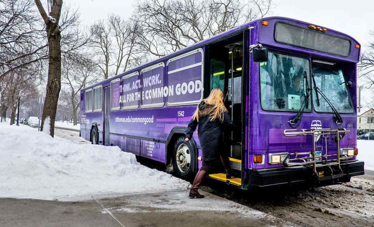 A student boards the St. Thomas shuttle bus February 4, 2016 on Summit Avenue near the Anderson Student Center. The bus is decked out in purple and "Think. Act. Work. All for the Common Good." logos.