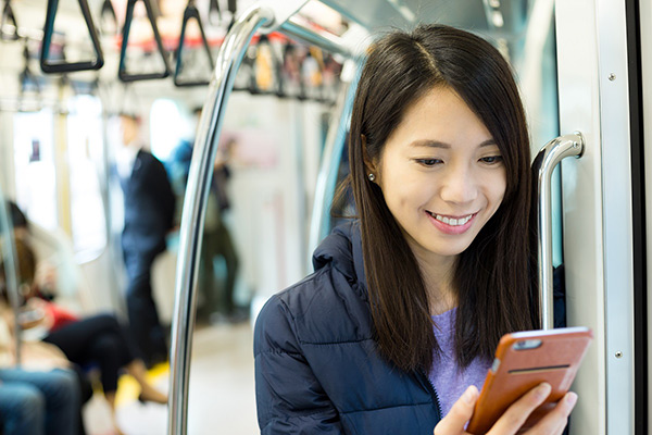 A woman smiles as she looks at her mobile phone inside of a public transit.