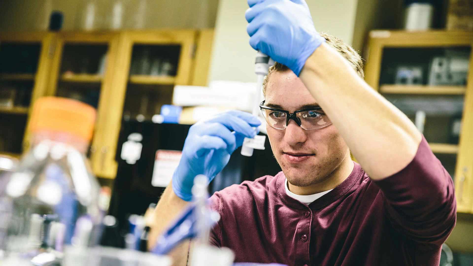 Chemistry major Jack Queenan holds a pipette and container in a lab in Owens Science Hall.