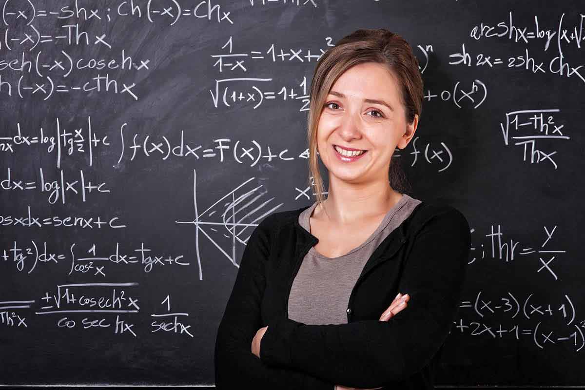 A female mathematics teacher posing in front of a blackboard.